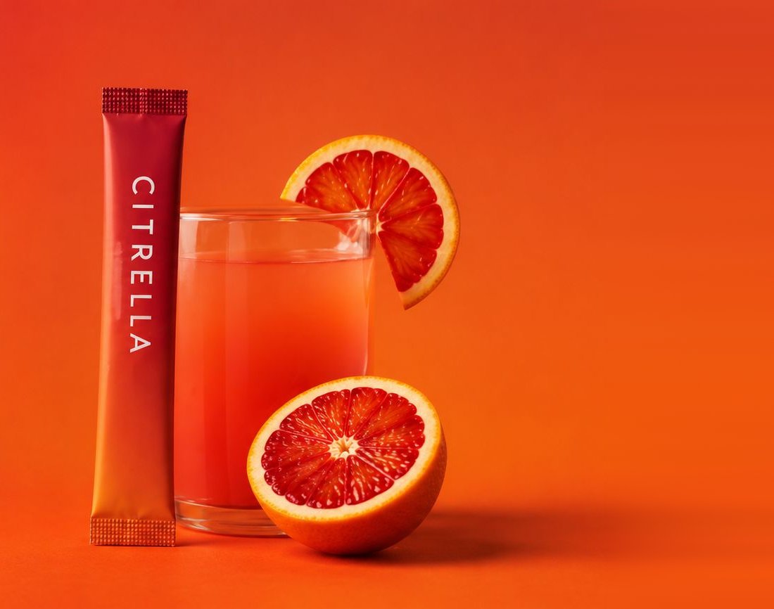 Citrella Slim Stick neben einem Glas Blutorangengetränk und zwei Orangenhälften
