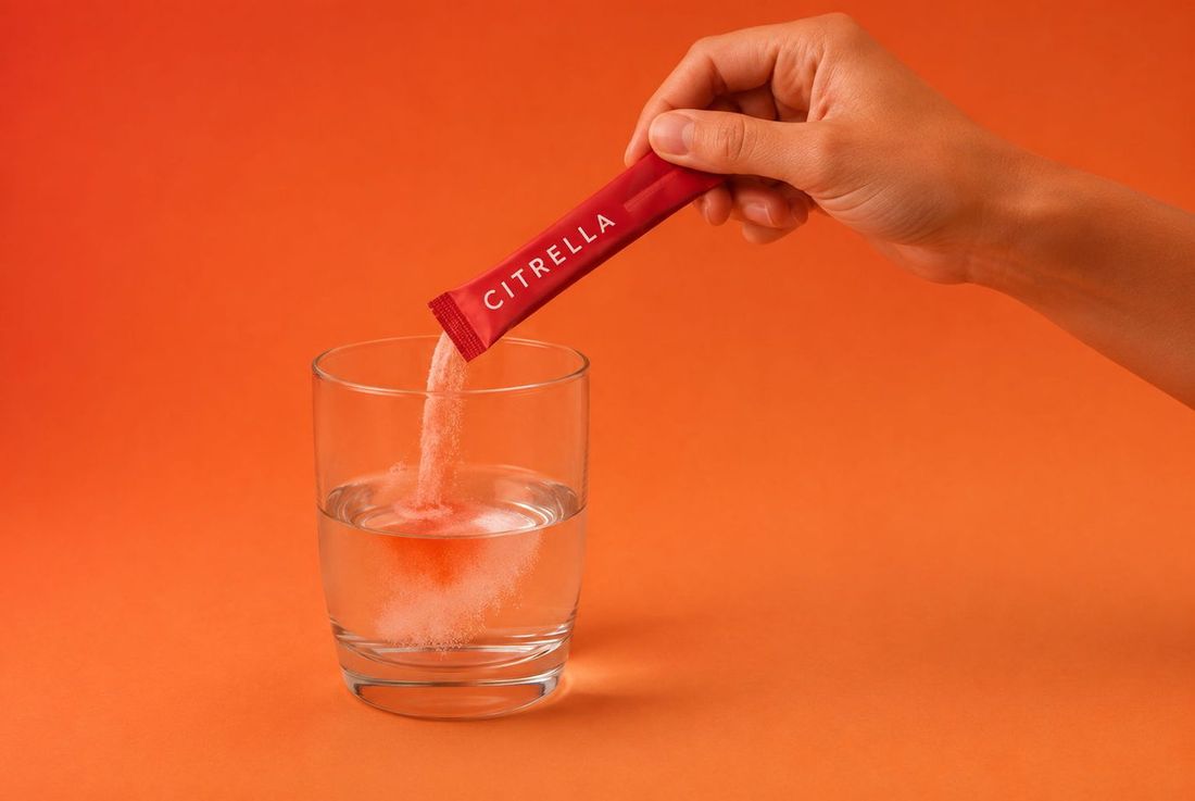 Hand schüttet das Pulver eines Citrella Slim Sticks in ein Glas Wasser